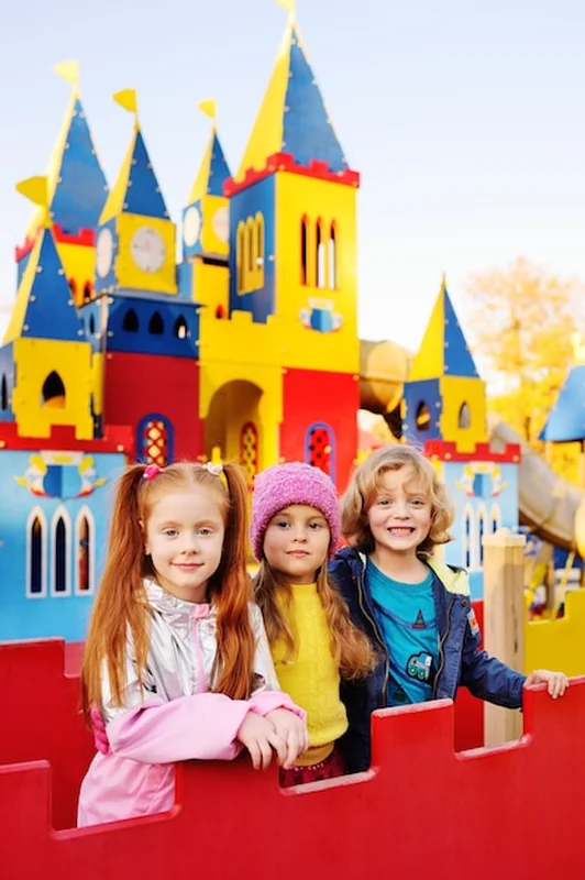Grupa dzieci bawi się w wesołym miasteczku przed kolorowym zamkiem