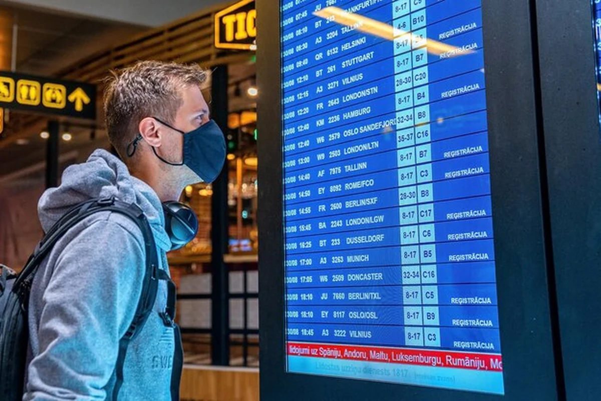 Młody mężczyzna z maską i walizką na lotnisku